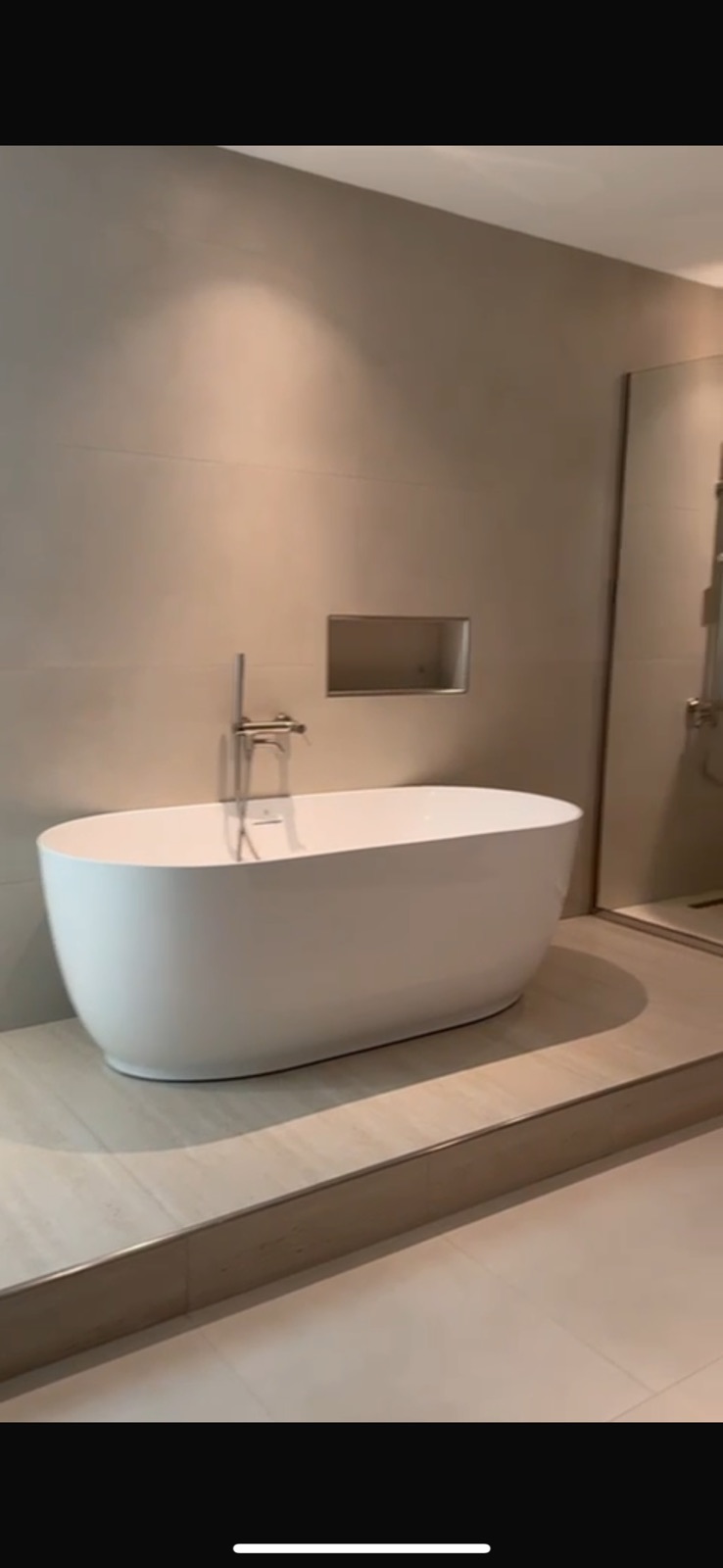 Freestanding bath on a raised travertine plinth against microcement walls with a recessed niche