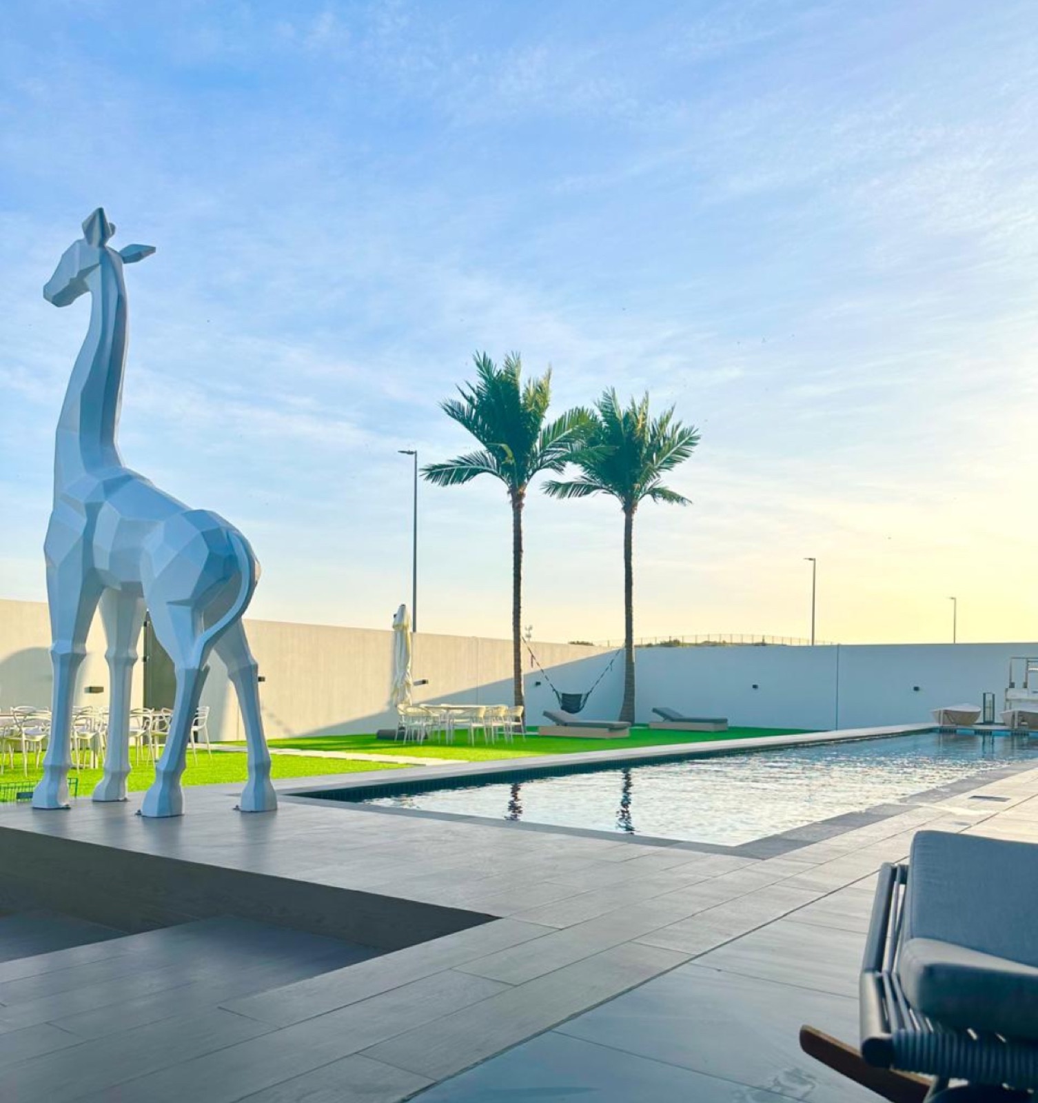 Long lap pool at sunset with a faceted sculpture, palms and lawn terrace