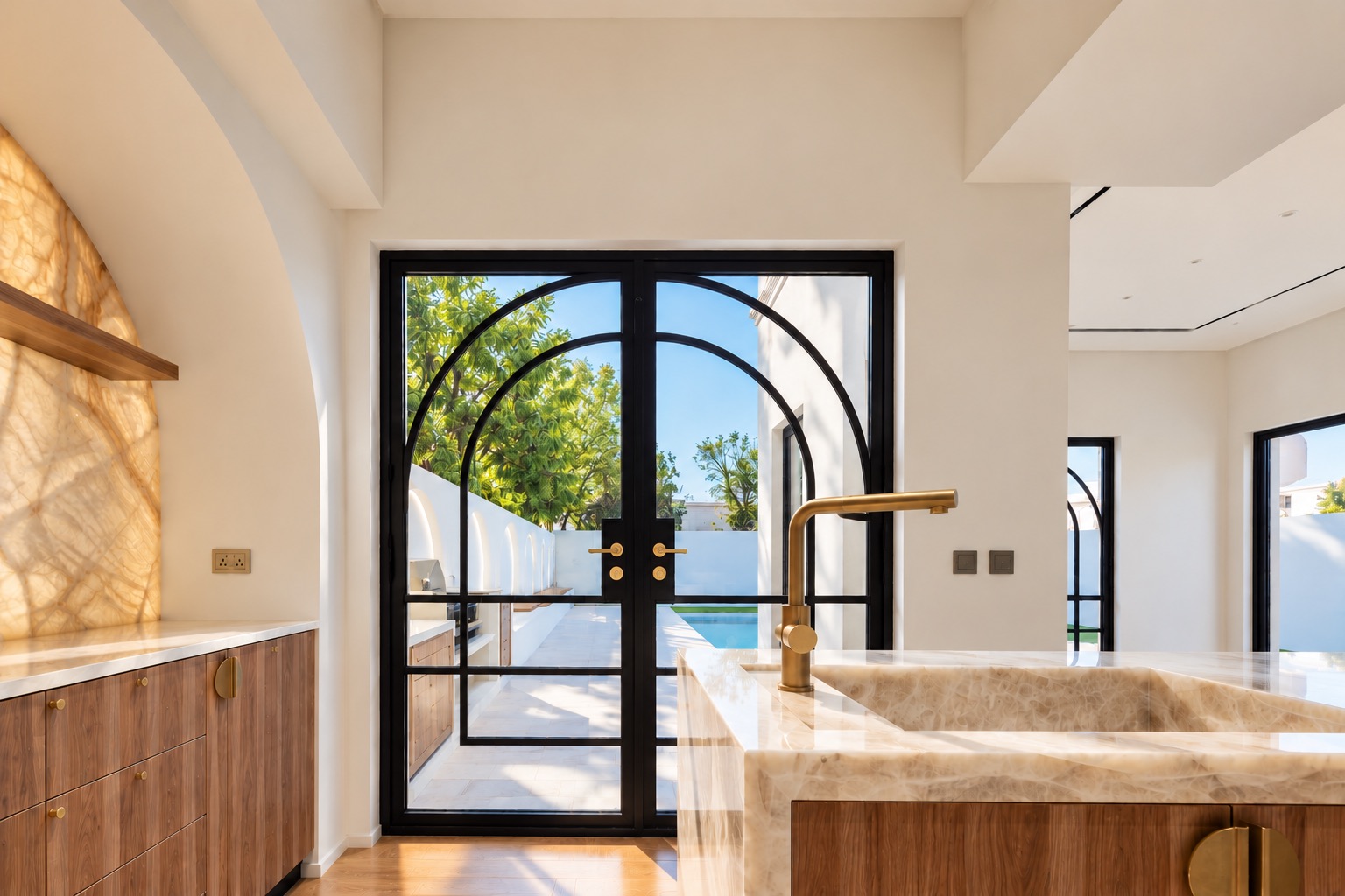 Kitchen with carved stone sink, brass tapware and arched steel doors opening to the pool
