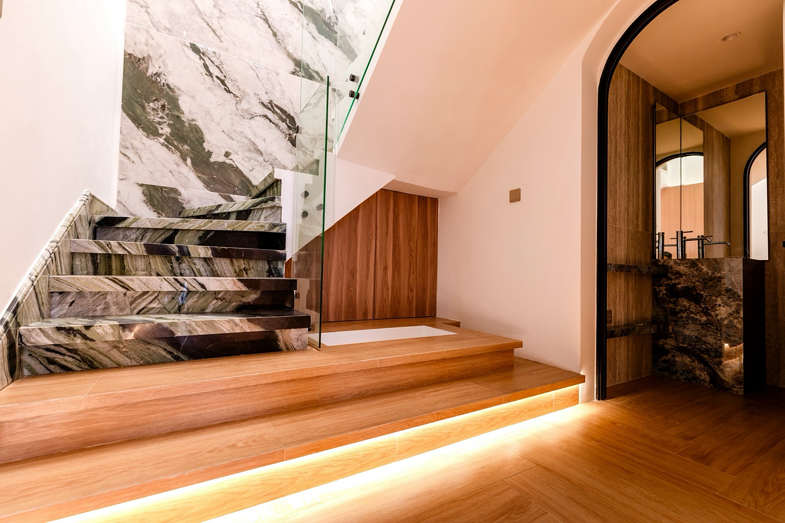 Staircase with book-matched marble treads, glass balustrade and concealed strip lighting